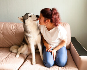 Young woman kissing her husky dog at home on the couch. life style