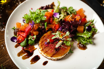 Goat cheese salad. Strawberry-melon salad with chilli, apple-orange sauce, fig jam on white plate. Delicious meat food closeup served on a table for lunch in modern cuisine gourmet restaurant