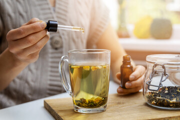 dietary supplements and vitamins - woman adding drop of cbd oil in cup of tea with pipette. anti...