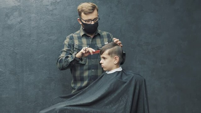 Epidemic of coronavirus infection COVID-19. Barber in protective medical mask cutting man's hair at home. Customer teenager Beauty service during quarantine
