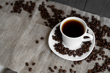 Coffee cup with roasted coffee beans on linen background. Mug of black coffe with scattered coffee beans. Fresh coffee beans.