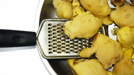 A closeup view of peeled gingers kept in a steel plate and a hand held grater ready to be grated.