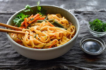 Noodles soup with carrots and parsley. Close up. Gray linen napkin. Wooden and concrete dark background. Egg noodles and Chinese sticks.