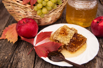 Basket with apples and grapes, a ceramic dish with honeycombs and honey on a wooden background.