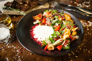 Crudo ham salad. Stracciatella and Grana Padano cheese, sundried tomato, fresh cucumber. Delicious healthy mixed greens food closeup served on a table for lunch in modern cuisine gourmet restaurant.