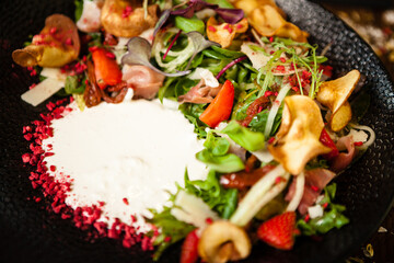 Crudo ham salad. Stracciatella and Grana Padano cheese, sundried tomato, fresh cucumber. Delicious healthy mixed greens food closeup served on a table for lunch in modern cuisine gourmet restaurant.