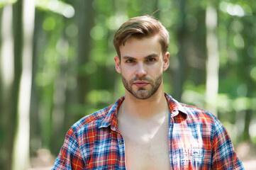 Young man with unshaven facial hair in open plaid shirt natural summer landscape outdoors, skin