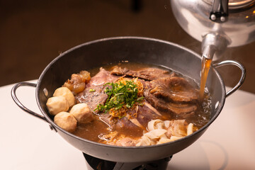 Chef pouring aromatic broth to fine sliced beef