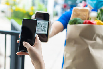 customer hand using digital mobile phone scan QR code paying for buying fresh food set bag from food delivery service man, express delivery, digital payment technology and fast food delivery concept