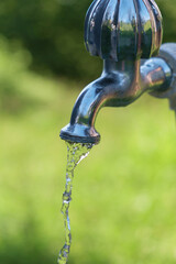 Pouring fresh water  from the metal tap with blurred nature background