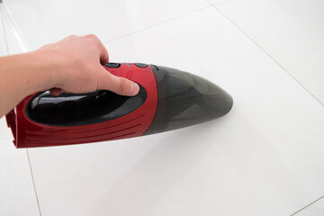 Red car vacuum cleaner, hand holding a car vacuum cleaner, cleaning the floor - obrazy, fototapety, plakaty