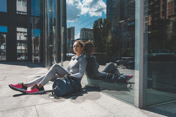 Young woman sits with her back against the glass wall