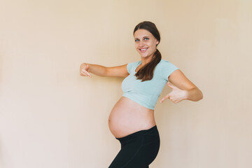 Young smiling pregnant woman in sportswear isolated on the beige background