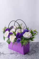 Festive bouquet of white eustoma and blue lisianthuses with delicate greenery lying in a purple cardboard bag.