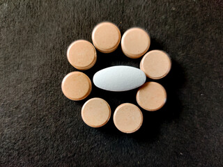White pills surrounded by orange tabletss. Isolated on black background.
