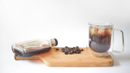Cold brew iced coffee in glass cup with ice cubes and coffee beans on white background.