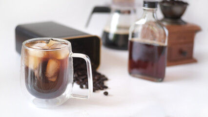 Cold brew iced coffee in glass cup with ice cubes on white table.