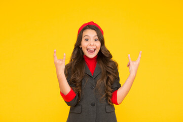 Happy small girl child in school uniform smile showing horns hand gestures yellow background, cool