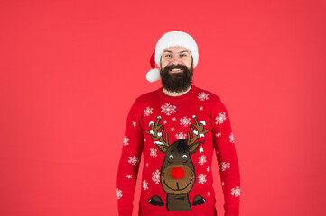 happy new year. cheerful hipster funny knitted sweater. warm clothes in cold winter weather. holiday season mood. bearded man santa hat red background. merry christmas. ready for xmas party