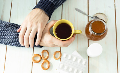 Medical care concept - hands holding cup with ginger honey and lemon tea with drugs, pills and spray on wood background