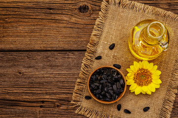 Sunflower oil in glass cruet with flower head and seeds in wooden bowl