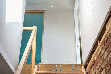 Steps leading to the loft space, unfinished loft extension project, plasterboarded walls, frame for the door, selective focus