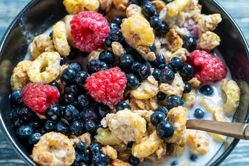 Muesli with raspberries, blueberries and flakes in a black bowl. Healthy food, healthy breakfast concept