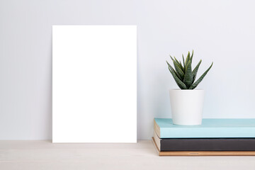 Blank mockup paper sheet copy space and plants in potted on book on wooden table, poster and invitation with empty on desk, card decoration your design or branding, simplicity and minimal, nobody.