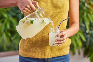 Woman pouring fresh lemonade from a pitcher into a drinking glass