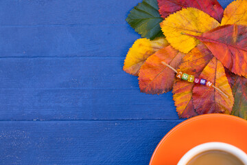 Fototapeta na wymiar Autumn Mood Background with Bright Colorful Leaves and Orange Cup of Coffee Latte on Wooden Blue Desk - Creative Composition Flat Lay, Still Life, Top View – Banner, Copy Space.