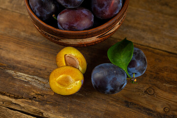 Blue plum in a bowl on a wooden table. Plums in a cut. Top view, place for text. Fruit background with copy space. Still life food.