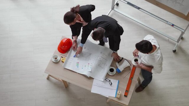 Top view of a team of engineers standing around their desks with paperwork and working equipment. They are discussing the work.