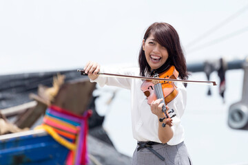 Beautiful asian woman hold violin on ship and nature background, in emotion feeling happy and...