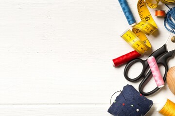 Collection of sewing tools with yarn, needles, scissors and tape measure over white wooden table...