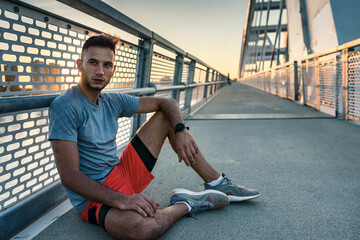 Obraz na płótnie Canvas Young handsome sporty jogger taking break from exercising outdoors in the sunset