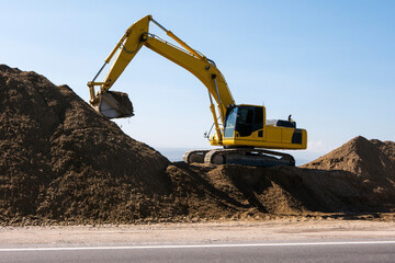 Yellow excavator loader machine during earthmoving works on blue sky background. Construction machinery, loading, lifting on job sites.