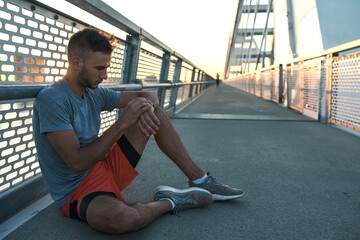 Young handsome sporty jogger taking break from exercising outdoors in the sunset