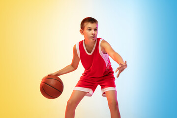 Full length portrait of young basketball player in uniform on gradient studio background. Teenager confident practicing with ball. Concept of sport, movement, healthy lifestyle, ad, action, motion.