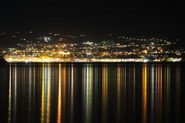 Porto Santo Stefano, Argentario, Italy by night. The colourful lights of the city reflect on the sea creating a beautiful light stripes pattern.
