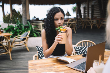 Delighted woman drinking cocktail in cafe
