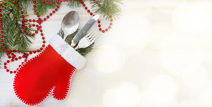Christmas banner.The idea of packaging Christmas gifts with a mitten, Cutlery: a spoon, knife and fork with Christmas pine branches. White wooden background, red beads, bokke.