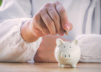 Closeup of senior man hand putting coin into piggy bank to saving money for retirement financial and pension annuity insurance. Concept for loan,property,financial,estate investment,taxes and bonus.