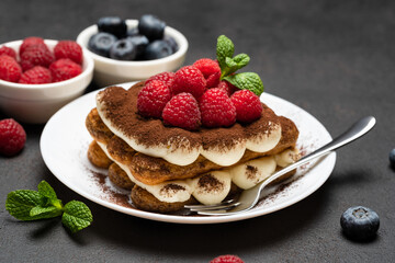 portion of Classic tiramisu dessert with raspberries and blueberries on dark concrete background
