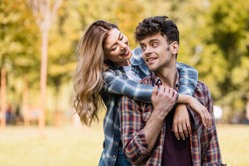 woman hugging man in checkered shirt in park