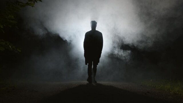 A silhouette of a man is walking through mist