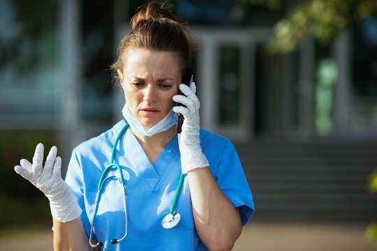 unhappy modern physician woman using phone outdoors near clinic