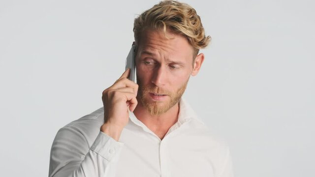 Handsome serious blond bearded businessman in shirt confidently talking on smartphone isolated. Business talk