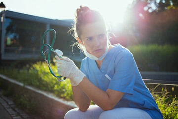 sad modern medical doctor woman sitting outdoors near clinic