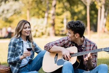 Fototapeta premium woman holding glass of red wine and looking at man playing acoustic guitar