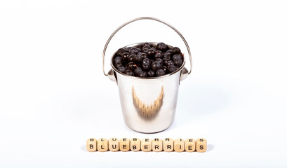 Ripe blueberries in a metal bucket, on wooden cubes the word blueberries on a white background